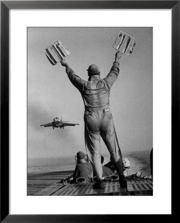 Shot Of A Man Using Hand Lights To Signal An Incoming Aircraft Towards The Carrier's Landing by Hank Walker Pricing Limited Edition Print image