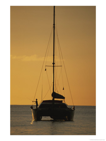 A Fisherman And His Sailboat Are Silhouetted Against The Yellow Sky by Michael Melford Pricing Limited Edition Print image