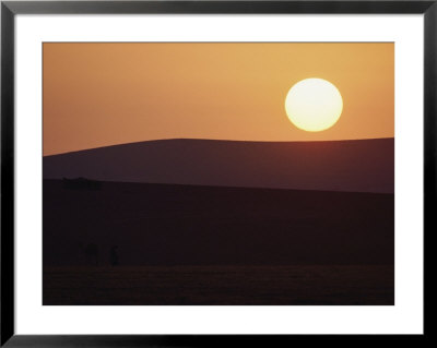 The Sun Hangs Over The Semi-Silhouetted Outline Of Two Large Hills by James L. Stanfield Pricing Limited Edition Print image
