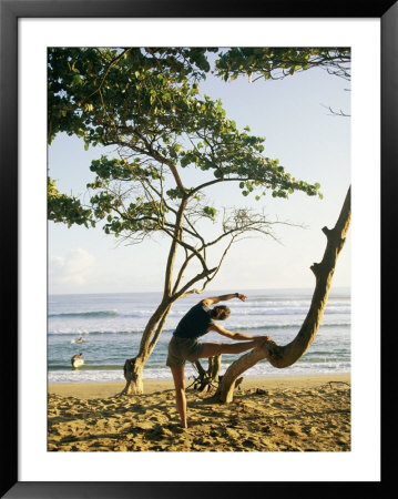 A Woman Stretches Her Body On A Small Tree At A Sandy Beach by Skip Brown Pricing Limited Edition Print image