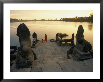 Two Buddhist Monks Sit At The Waters Edge At A Lake Temple In The Angkor Wat Complex by Paul Chesley Pricing Limited Edition Print image