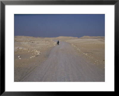 A Dark-Robed Egyptian Contrasted Against The Bright Desert Landscape Near Saqqara by Stephen St. John Pricing Limited Edition Print image