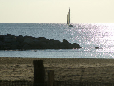 Sailboat In The Mediterranean, With A Beach And Rocks, Foreground, La Grande Motte, France by Stephen Sharnoff Pricing Limited Edition Print image