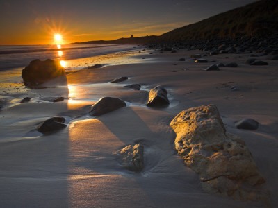 Early Morning Sunshine On Sandstone Boulders, Dunstanburgh Beach, Northumberland, England by Adam Burton Pricing Limited Edition Print image