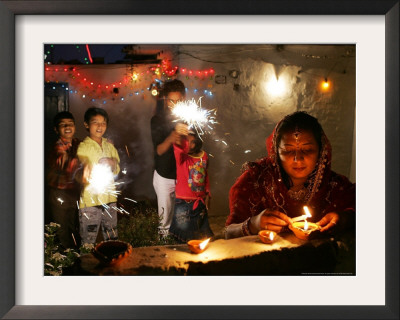 A Woman Lights Earthen Lamps As Children Ignite Firecrackers In New Delhi by Manish Swarup Pricing Limited Edition Print image