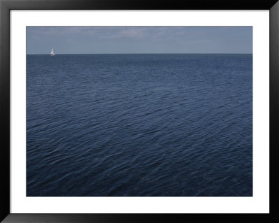 A Wide And Empty Blue Ocean Is Punctuated By A Single Tiny Sailboat by Stephen St. John Pricing Limited Edition Print image