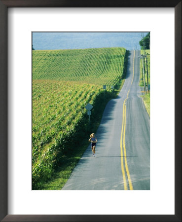 A Woman Jogs Down A Country Road Alongside A Field Of Corn by Skip Brown Pricing Limited Edition Print image
