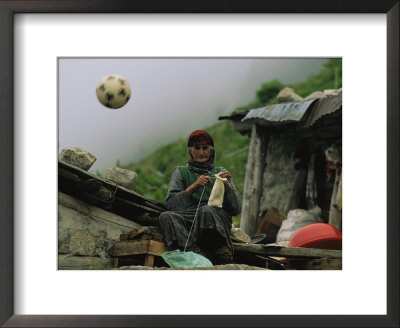 A Soccer Ball Flies Over The Head Of Woman Who Is Knitting Outdoors by Randy Olson Pricing Limited Edition Print image