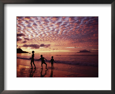 Sunset Reddens A Cloudy Sky As Silhouetted Children Play On The Beach by Steve Raymer Pricing Limited Edition Print image