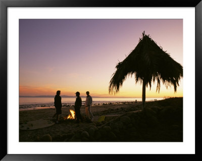 Surfers Stand Near A Fire And Palapa At Hammonds Beach At Sunset by Rich Reid Pricing Limited Edition Print image