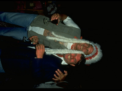 Chevy Chase In Native American Headdress, Arm Around Rolling Stone Owner Jann Wenner At Party by Dave Allocca Pricing Limited Edition Print image