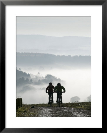 Two Mountain Bikes Climbing Up Hill, Silhouetted Against Mist, Newlands Corner, Surrey, England by John Miller Pricing Limited Edition Print image