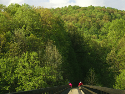 Cyclists Cross A Bridge On The Youghiogheny River Trail by Joel Sartore Pricing Limited Edition Print image