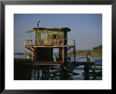 A Man Sits On A Pier Near A Dilapidated Shack by Raymond Gehman Pricing Limited Edition Print image