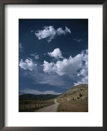 Dirt Road To Ranch Through Desert Hills Against A Blue Cloudy Sky by Todd Gipstein Pricing Limited Edition Print image