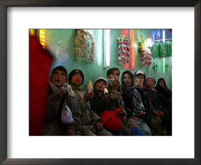 Afghan Boys Watch A Movie On A Television, Unseen, As They Eat Ice Cream At An Ice Cream Shop by Rodrigo Abd Pricing Limited Edition Print image