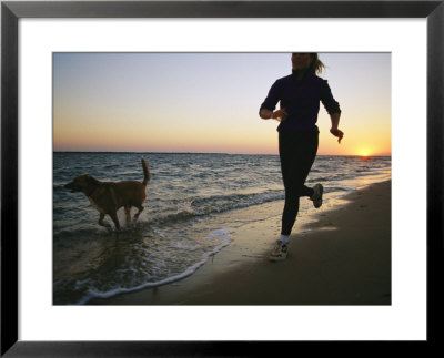 A Woman And Her Dog Run On The Beach At Sunset by Skip Brown Pricing Limited Edition Print image
