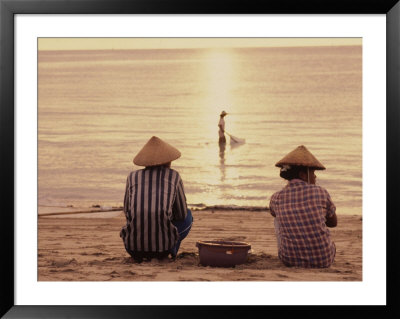 Women Sitting On Beach With Man Fishing, Indonesia by Bonnie Kamin Pricing Limited Edition Print image