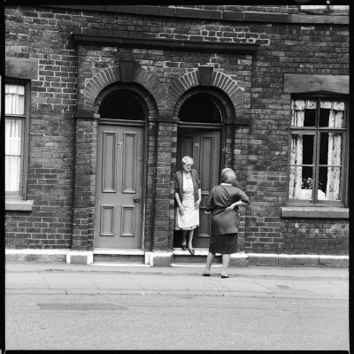 Two Women Gossip On The Doorstep In A Sheffield Street by Henry Grant Pricing Limited Edition Print image