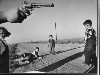 A Toy Six-Shooter Pistol And Boys Lying In Dirt Road; A Game Of Cops And Robbers On The Prairie by Howard Sochurek Pricing Limited Edition Print image