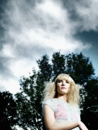 A Young, Blond Woman Against A Background Of Trees And Sky, Iceland by Atli Mar Pricing Limited Edition Print image