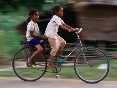 Girls Riding Bicycle In Bavel Village, Battambang, Cambodia by Jerry Galea Pricing Limited Edition Print image