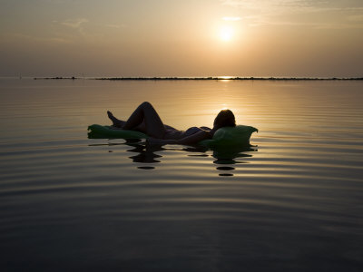 Woman Laying On Raft At Sunset In The Ocean by Scott Stulberg Pricing Limited Edition Print image