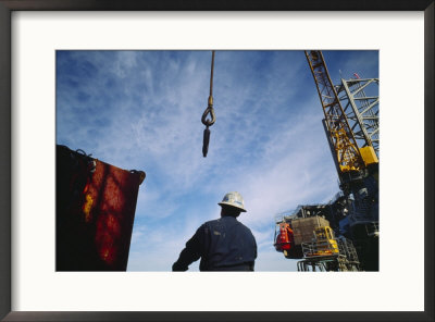 A Worker Uses A Crane And Hoist To Lift A Large Container Onto An Oil Rig by Eightfish Pricing Limited Edition Print image