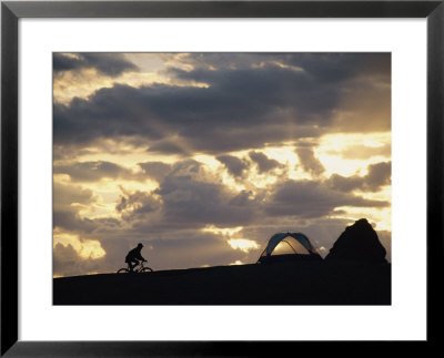 A Mountain Biker Cycles Toward Tents At A Campsite by Dugald Bremner Pricing Limited Edition Print image