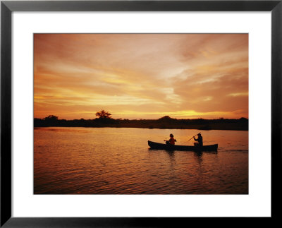 A Couple Rowing A Canoe Is Silhouetted Against A Gorgeous Sunset by Barry Tessman Pricing Limited Edition Print image