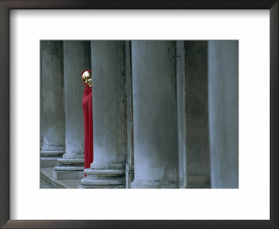 Carnival Model In Red Cape And Gold Mask Peering From Columns In St. Mark's Square, Veneto, Italy by Lee Frost Pricing Limited Edition Print image
