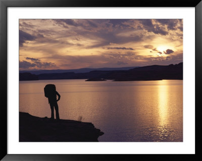 A Hiker Pauses For Reflection Alongside Lake Powell At Sunset by Gordon Wiltsie Pricing Limited Edition Print image