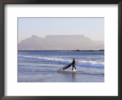 Young Woman Surfer Enters The Water Of The Atlantic Ocean With Table Mountain In The Background by Yadid Levy Pricing Limited Edition Print image