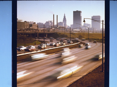 Blurred Traffic On Curving Stretch Of Highway With Skyscrapers In Distance by Ralph Crane Pricing Limited Edition Print image