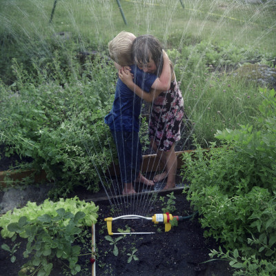Side Profile Of A Girl And A Boy Hugging Each Other Near A Sprinkler by Mikael Andersson Pricing Limited Edition Print image