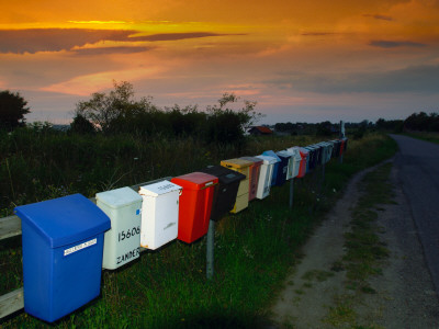 A Row Of Colourful Mailboxes On A Fence By A Gravel Road by Christian Lagerek Pricing Limited Edition Print image