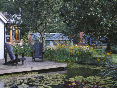 View Across Lily Pool To Deck With Adirondack Chairs, In The Background Is The Main Greenhouse by Clive Nichols Pricing Limited Edition Print image