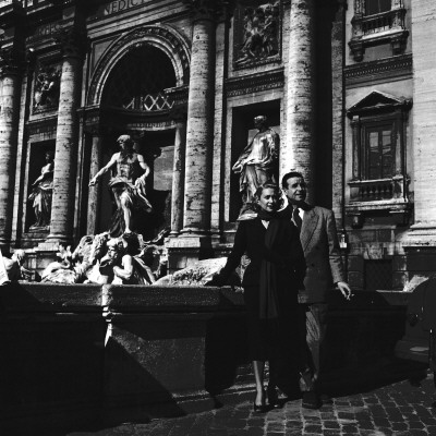 Martine Carol With Christian-Jaque Standing By The Trevi Fountain In Rome by Benno Graziani Pricing Limited Edition Print image