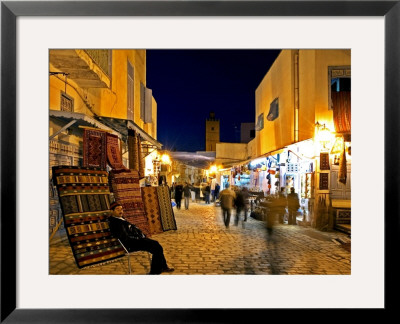 People Strolling Along Cobblestone Street Past Carpet Seller At Twilight, Kairouan, Tunisia by Bethune Carmichael Pricing Limited Edition Print image