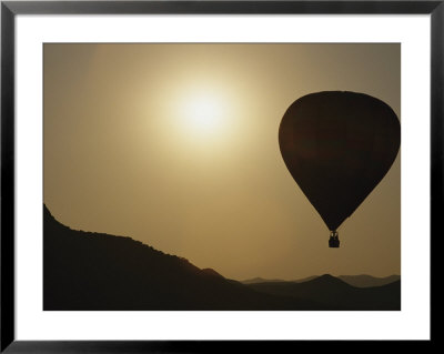 A Hot Air Balloon Rises Above A Hilly Landscape At Sunrise by Raul Touzon Pricing Limited Edition Print image