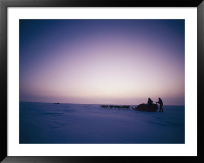 Huskies Carry A Sled Across The Ice At Twilight by Gordon Wiltsie Pricing Limited Edition Print image