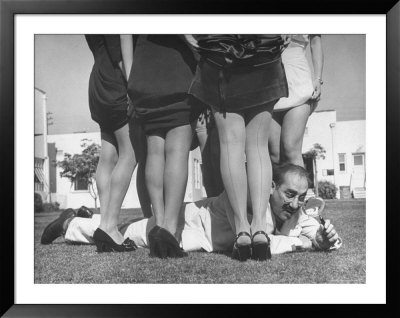 Comedian Groucho Marx Studies While Lying In The Center Of Women Showing Off Their Shapely Legs by Bob Landry Pricing Limited Edition Print image