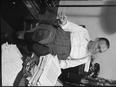 Writer Damon Runyon Sitting With Feet Up At Work-Piled Desk. Typewriter And Telephone Nearby by Gjon Mili Pricing Limited Edition Print image