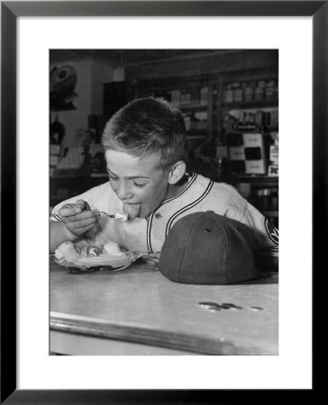 Boy Wearing Baseball Uniform Eating Banana Split At Soda Fountain Counter by Joe Scherschel Pricing Limited Edition Print image