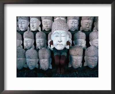 A Shy Young Boy Hiding Behind One Of Many Carved Wooden Faces In A Shop Front, Indonesia by Adams Gregory Pricing Limited Edition Print image
