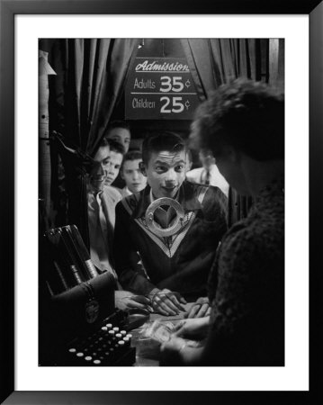 Teenage Boy Peering Into Window Of Ticket Booth At A Movie Theater by Yale Joel Pricing Limited Edition Print image