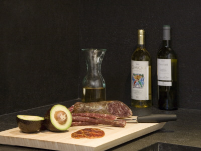Kitchen Detail - Avocados And Salami On Chopping Board With Bottles Of White Wine by Ton Kinsbergen Pricing Limited Edition Print image