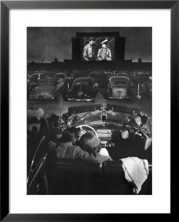 Young Couple Snuggling In Convertible As They Watch Large Screen Action At A Drive-In Movie Theater by J. R. Eyerman Pricing Limited Edition Print image