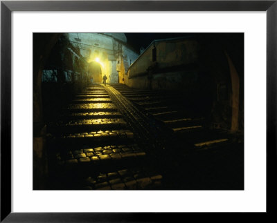 Silhouetted Person Walking Up Lamp-Lit Cobblestone Street, Sighisoara, Romania by David Greedy Pricing Limited Edition Print image
