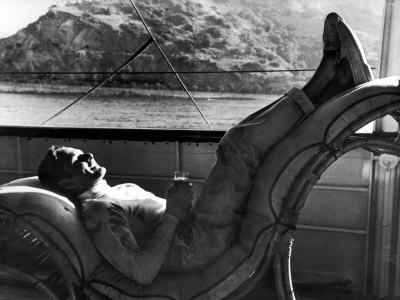Actor Errol Flynn Relaxing On A Reclining Chair On The Deck Of A Boat Passing Beside A Mountain by Peter Stackpole Pricing Limited Edition Print image